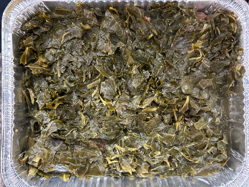 A large aluminum pan filled with dark green, cooked collard greens, a soul food staple.