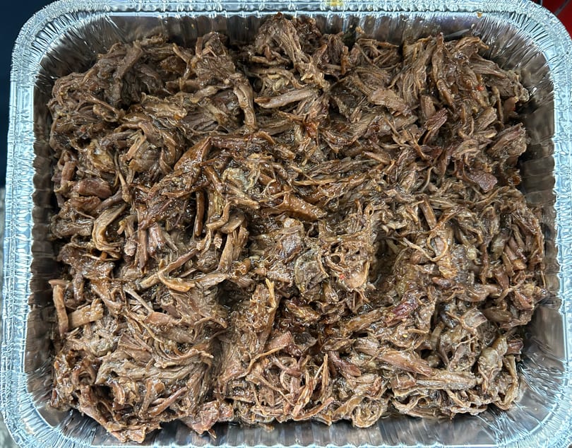 Close-up of shredded, saucy soul food meat in a large aluminum pan.
