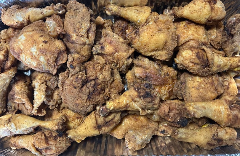 A large catering tray filled with golden-brown, crispy fried chicken pieces from Mittie Mae's Corner Market.